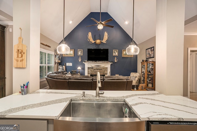 kitchen featuring a stone fireplace, light stone counters, sink, ceiling fan, and decorative light fixtures