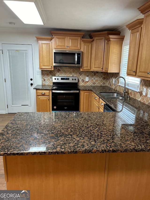 kitchen with stainless steel appliances, sink, kitchen peninsula, dark stone counters, and light wood-type flooring