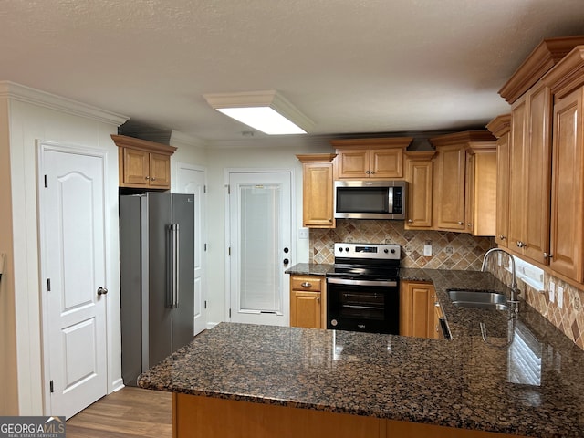 kitchen with stainless steel appliances, light hardwood / wood-style floors, sink, kitchen peninsula, and dark stone countertops