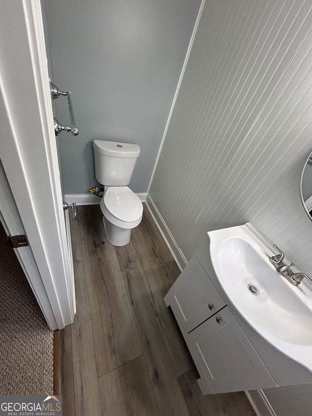 bathroom with toilet, wood walls, hardwood / wood-style flooring, vanity, and crown molding