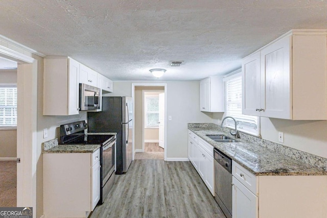 kitchen with white cabinets, a wealth of natural light, stainless steel appliances, and light hardwood / wood-style flooring