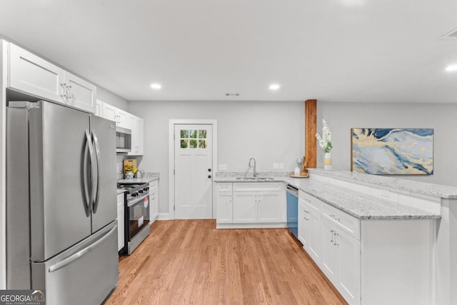 kitchen with light stone counters, stainless steel appliances, white cabinetry, light hardwood / wood-style floors, and kitchen peninsula