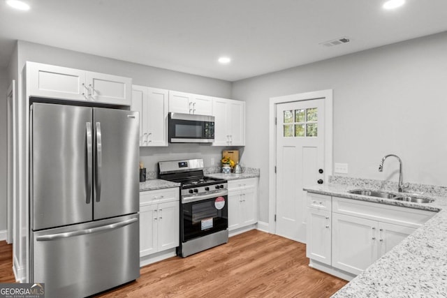 kitchen with stainless steel appliances, sink, light stone countertops, light hardwood / wood-style flooring, and white cabinets