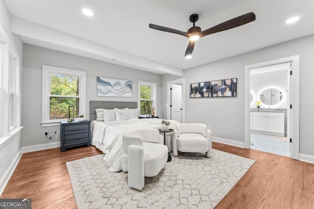 bedroom with ensuite bath, ceiling fan, multiple windows, and wood-type flooring