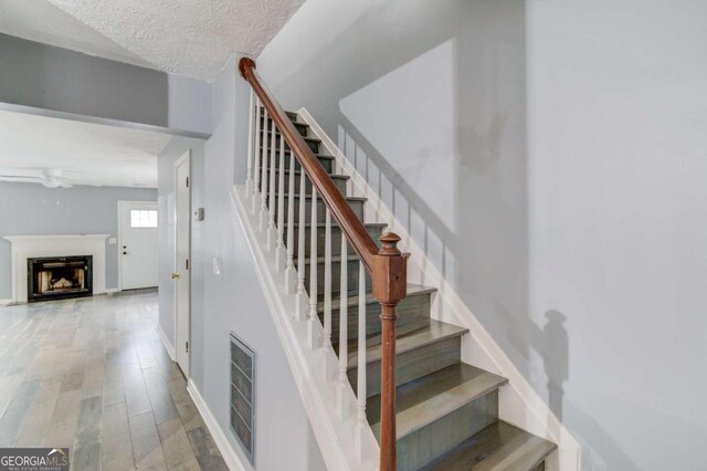 stairs featuring ceiling fan, wood-type flooring, and a textured ceiling