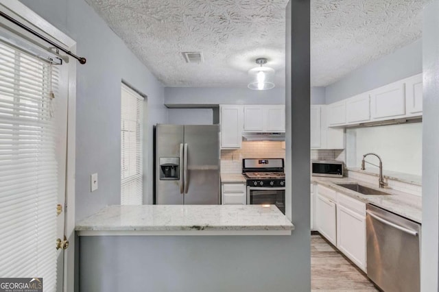 kitchen featuring stainless steel appliances, light stone countertops, sink, light hardwood / wood-style floors, and white cabinets