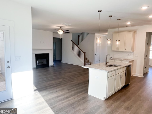 kitchen with light stone countertops, tasteful backsplash, sink, decorative light fixtures, and a center island with sink