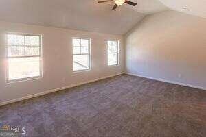 carpeted empty room featuring a wealth of natural light, ceiling fan, and vaulted ceiling