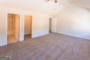 unfurnished bedroom with ensuite bath, ceiling fan, vaulted ceiling, and dark colored carpet