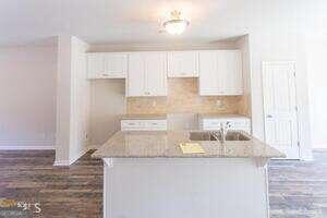 kitchen featuring a kitchen island with sink, white cabinets, sink, light stone counters, and dark hardwood / wood-style flooring