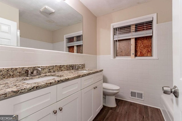 bathroom featuring toilet, tile walls, a textured ceiling, hardwood / wood-style flooring, and vanity