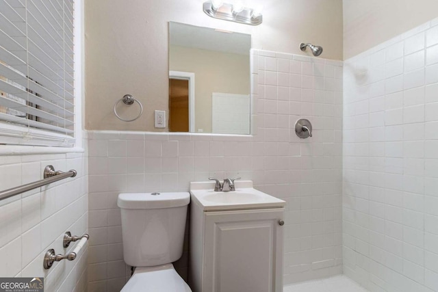 bathroom with tile walls, tiled shower, vanity, and toilet