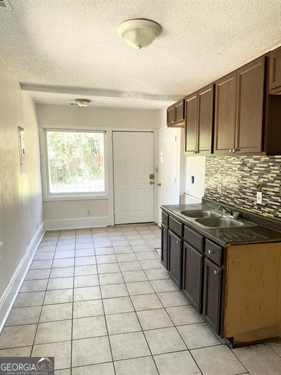 kitchen featuring decorative backsplash, a textured ceiling, sink, light tile patterned flooring, and dark brown cabinets