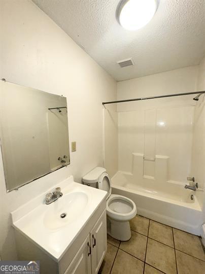 full bathroom with tile patterned flooring, a textured ceiling,  shower combination, vanity, and toilet