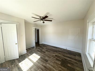 unfurnished bedroom featuring multiple windows, dark wood-type flooring, and ceiling fan