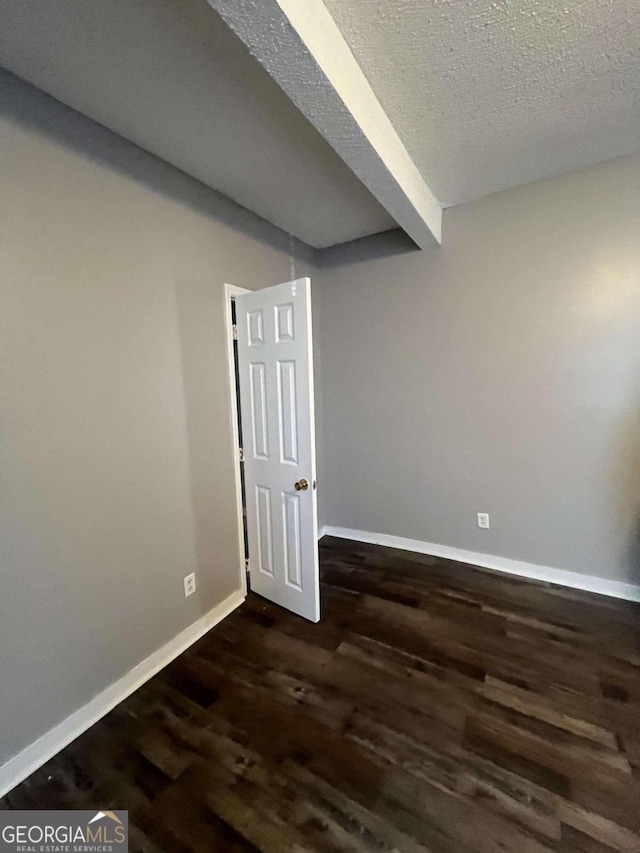 empty room with dark hardwood / wood-style flooring, beamed ceiling, and a textured ceiling