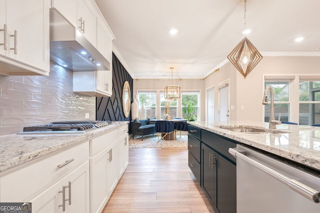 kitchen with a sink, stainless steel appliances, ventilation hood, white cabinetry, and pendant lighting