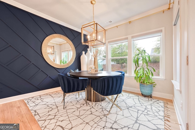 dining space featuring wooden walls, a notable chandelier, ornamental molding, and light hardwood / wood-style flooring