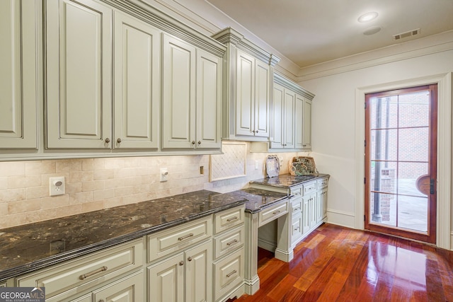 kitchen featuring cream cabinets, ornamental molding, dark stone countertops, dark wood-type flooring, and decorative backsplash