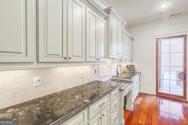 kitchen with hardwood / wood-style floors, tasteful backsplash, crown molding, and dark stone countertops