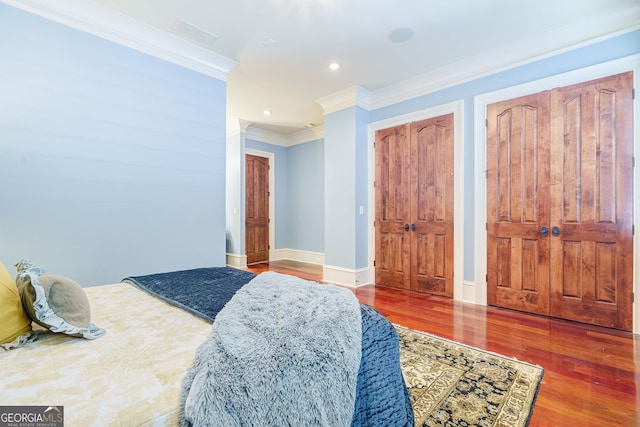 bedroom featuring ornamental molding, wood-type flooring, and two closets