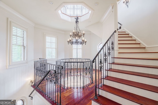 stairs with wood-type flooring, an inviting chandelier, and ornamental molding