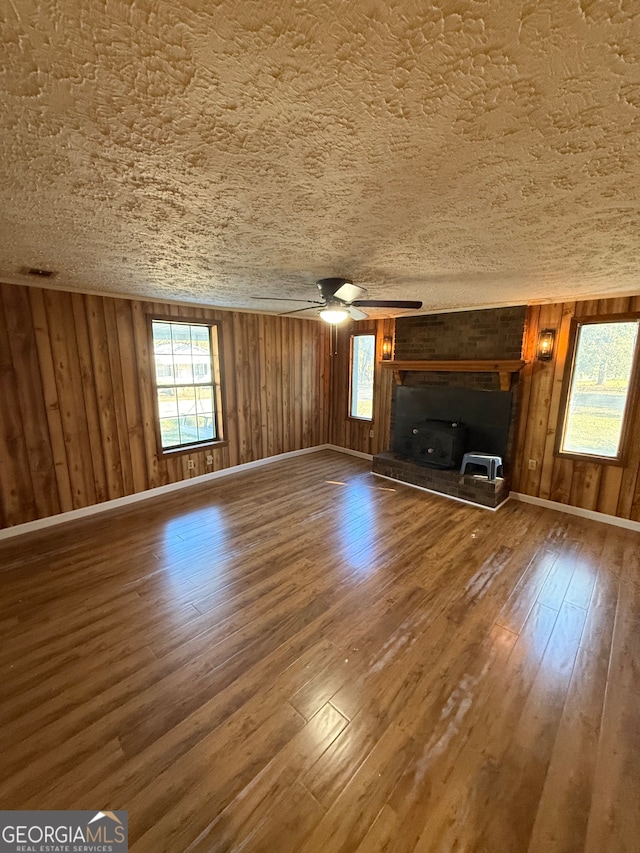 unfurnished living room featuring ceiling fan, wood walls, wood-type flooring, and a textured ceiling