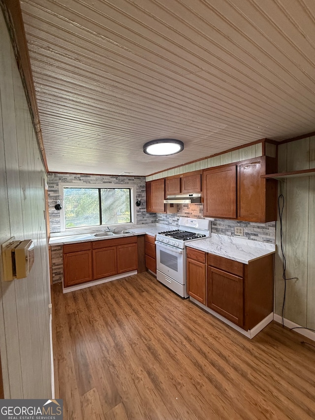 kitchen featuring gas range gas stove, wooden walls, sink, and light wood-type flooring