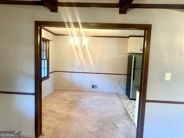 spare room with an inviting chandelier, light colored carpet, and beam ceiling