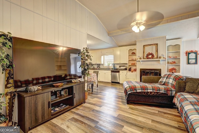 living room with ceiling fan, wooden walls, light wood-type flooring, and lofted ceiling