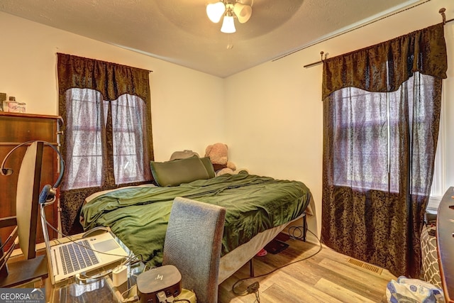 bedroom with ceiling fan, a textured ceiling, and light hardwood / wood-style floors