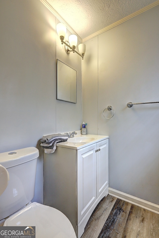 bathroom with ornamental molding, a textured ceiling, wood-type flooring, vanity, and toilet