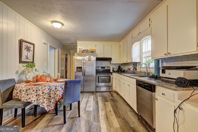 kitchen with sink, appliances with stainless steel finishes, ornamental molding, dark stone countertops, and dark wood-type flooring