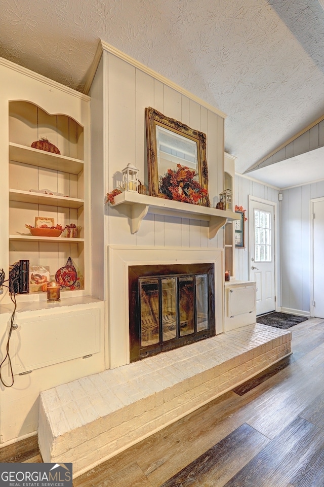 living room with hardwood / wood-style flooring, a textured ceiling, lofted ceiling, a brick fireplace, and built in features