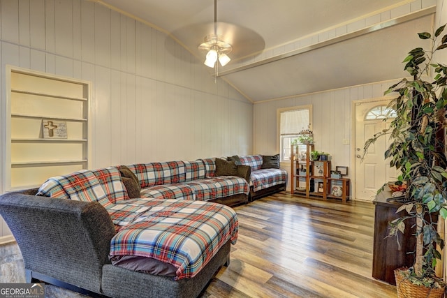 living room featuring built in shelves, wooden walls, hardwood / wood-style floors, lofted ceiling, and ceiling fan