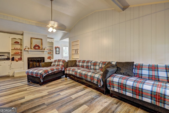 living room featuring built in features, wood walls, light hardwood / wood-style floors, lofted ceiling, and ceiling fan