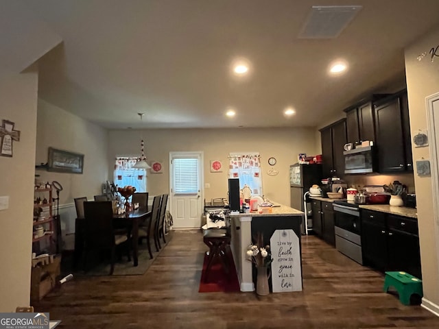 kitchen with a breakfast bar, dark wood-type flooring, stainless steel appliances, and an island with sink