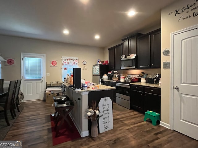 kitchen with a kitchen bar, light stone counters, stainless steel appliances, dark wood-type flooring, and an island with sink