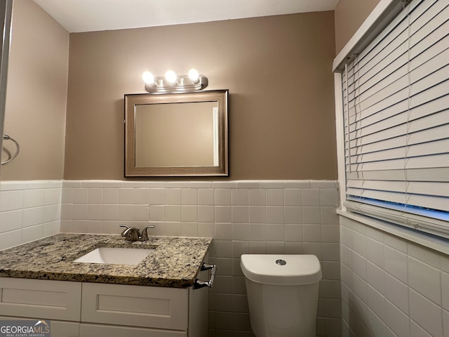 bathroom with toilet, vanity, and tile walls