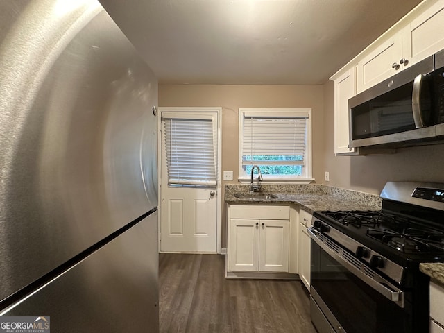 kitchen featuring stainless steel appliances, dark wood-type flooring, dark stone counters, white cabinets, and sink