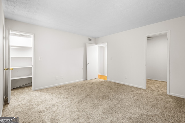 unfurnished bedroom with light colored carpet, a spacious closet, a textured ceiling, and a closet