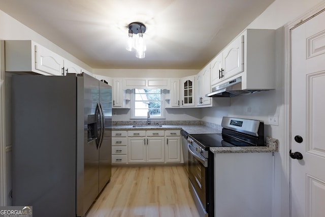 kitchen with appliances with stainless steel finishes, sink, stone counters, white cabinets, and light hardwood / wood-style floors