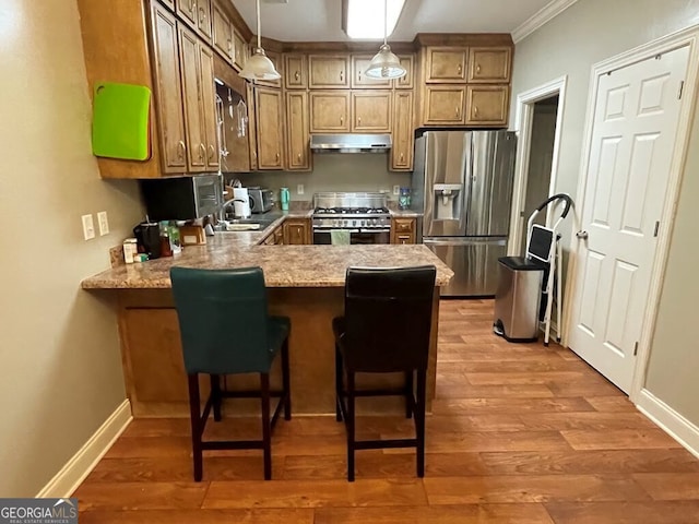 kitchen with stainless steel appliances, kitchen peninsula, hardwood / wood-style flooring, crown molding, and pendant lighting