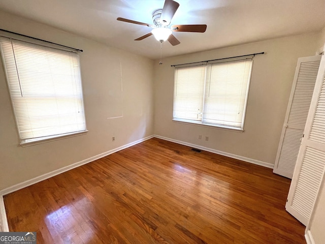 unfurnished bedroom with a closet, multiple windows, ceiling fan, and dark hardwood / wood-style floors