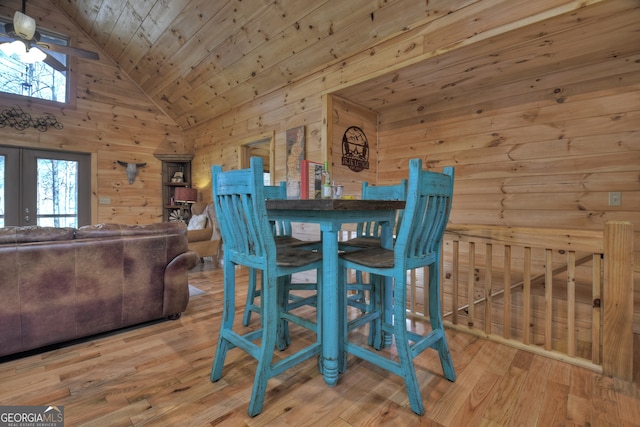 dining room featuring french doors, wood ceiling, wooden walls, high vaulted ceiling, and light hardwood / wood-style flooring