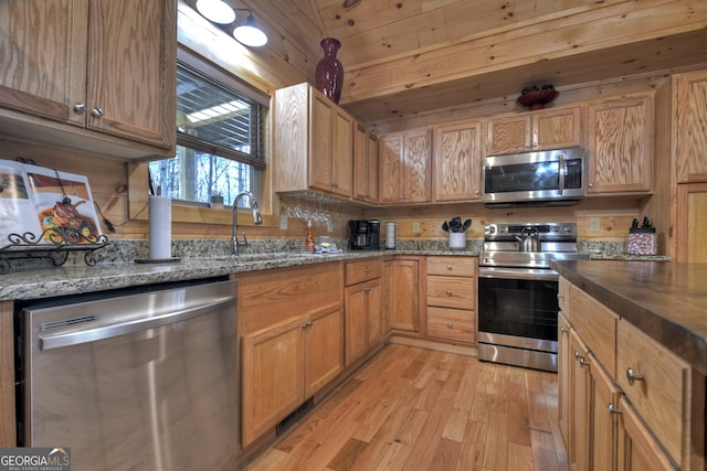 kitchen with stainless steel appliances, wooden ceiling, sink, dark stone counters, and light hardwood / wood-style flooring