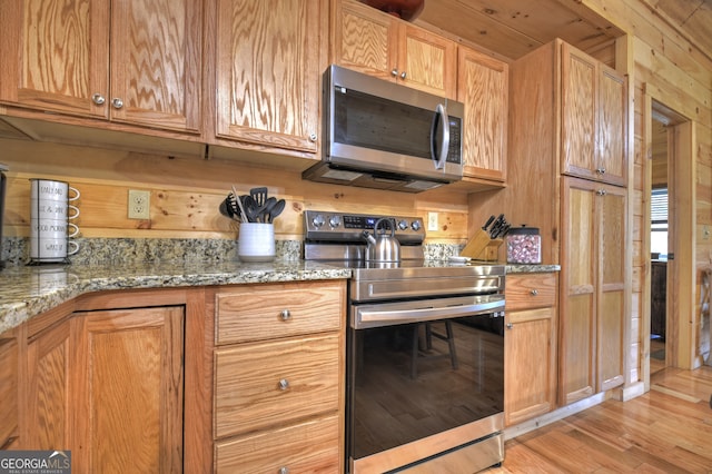 kitchen featuring light wood-type flooring, light stone countertops, wooden walls, and stainless steel appliances