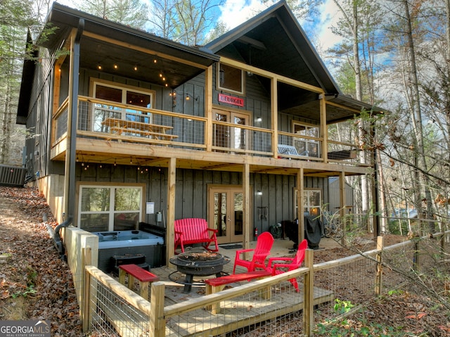 rear view of property with a hot tub, central AC unit, french doors, a fire pit, and a balcony