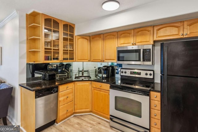 kitchen with ornamental molding, appliances with stainless steel finishes, sink, dark stone countertops, and light hardwood / wood-style flooring