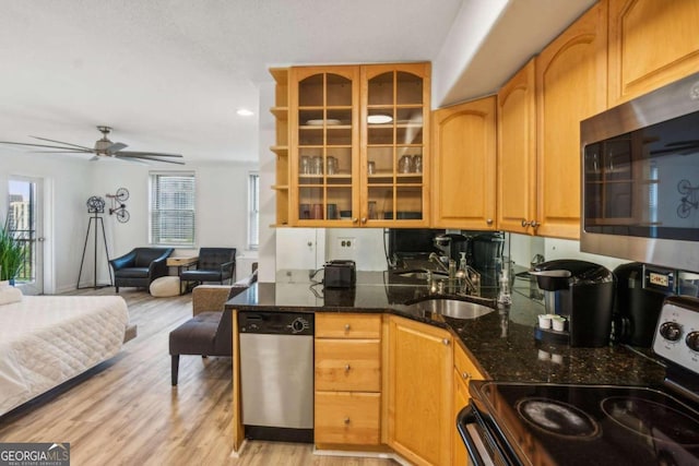 kitchen with appliances with stainless steel finishes, sink, dark stone countertops, ceiling fan, and light hardwood / wood-style flooring